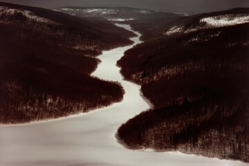Serene snowy river winding through forested hills in winter landscape