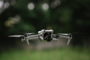 A gray drone with green lights hovers mid-air, indicating its active flight for surveillance or photography.