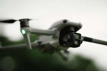 A gray drone with green lights hovers mid-air, indicating its active flight for surveillance or...
