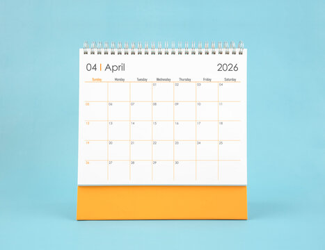 April 2026 white desk calendar on blue color background. Planning and goals concepts.