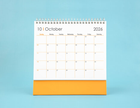 October 2026 white desk calendar on blue color background. Planning and goals concepts.