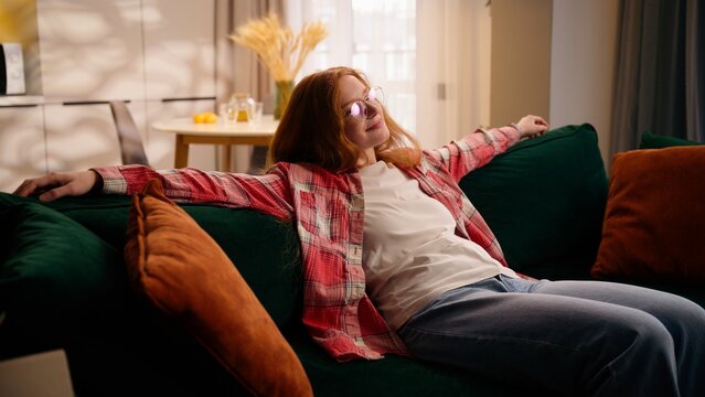 Joyful Caucasian girl female woman happy smiling falling couch cozy home sitting on sofa rest chilling at living room satisfied lady relaxing own rent apartment domestic relocation moving day mortgage - Powered by Adobe