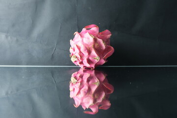 Fresh pink dragon fruit placed on a reflective glass surface with a dark backdrop, creating a...