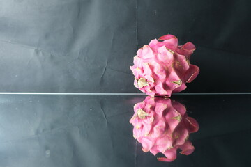 Fresh pink dragon fruit placed on a reflective glass surface with a dark backdrop, creating a...