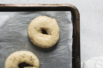 Overhead view of freshly boiled bagel dough, top view of raw homemade bagels on parchment lined baking sheet
