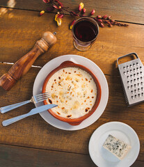 Flat Lay of Lasagna with Pepper Grinder, Wine, Cheese, and Fork on Wooden Table