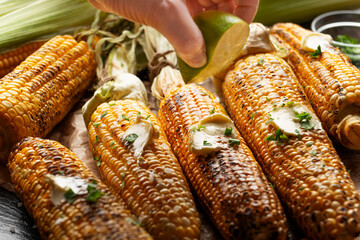 Grilled sweetcorn cobs with butter on the table being seasoned by lime juice closeup low angle view