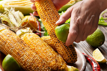 Female hands rubbing a roasted sweet corn cob with lime