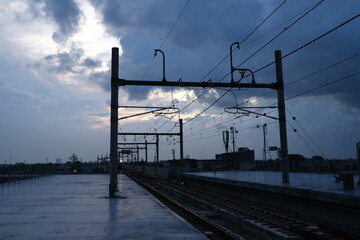 Electric railway tracks at sunset with overhead power lines silhouetted against a moody, cloudy sky