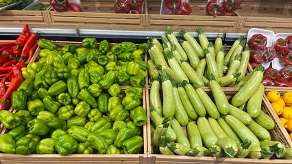 Fresh green bell peppers and zucchini are displayed in wooden crates in the vegetable section of a...