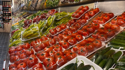 Tomatoes, peppers, and cucumbers wrapped in plastic film and displayed in the vegetable section of...