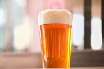 Glass of drafted fresh beer with thick head of foam on a table