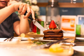 Woman cutting chocolate cake with strawberry on a plate.