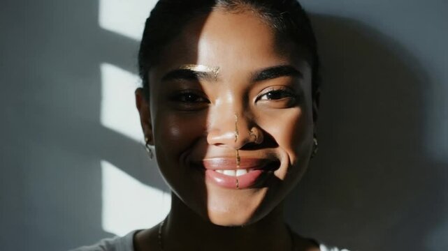 A young African woman with short hair and dimples smiles softly. Light and shadow create a striking contrast on her face, celebrating Dimples Day..