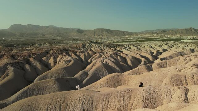White and black angels walking across barren hilly terrain, representing opposing forces and spiritual balance in stark, symbolic journey