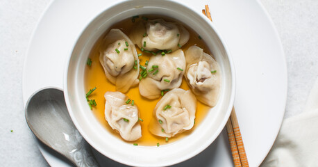 Overhead view of wonton soup in a white ceramic bowl, clear soup with dumplings in a white soup bowl
