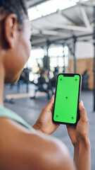 Girl hand holding a smartphone with empty green screen chromakey at the gym.
