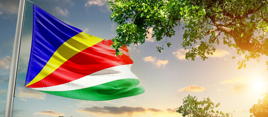 Seychelles national flag waving in the sky behind the tree. The flag blow in beautiful sunlight. Seychelles national flag for independence day.