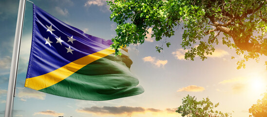Solomon Islands national flag waving in the sky behind the tree. The flag blow in beautiful sunlight. Solomon Islands national flag for independence day.
