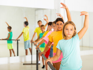 Concentrated assiduous preteen girl working near ballet barre during group choreography class .