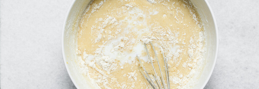 Overhead view of flour being mixed into cake batter, top view of vanilla cake batter being mixed, process of making vanilla cake