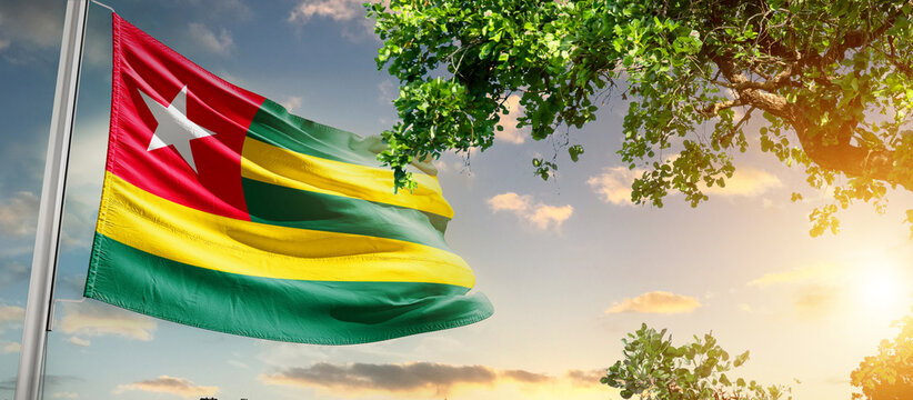 Togo national flag waving in the sky behind the tree. The flag blow in beautiful sunlight. Togo national flag for independence day. - Powered by Adobe