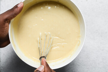 Overhead view of cake batter being whisked, top view of vanilla cake batter being mixed, process of...