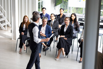 Fototapeta premium Back view speaking training in seminar : Senior caucasian business man leader in seminar, speaking on business training with group of diverse people company employees in meeting room