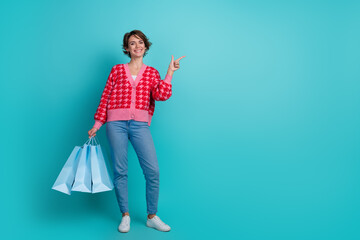 Full length photo of cute sweet lady wear red cardigan holding bargains pointing emtpy space isolated turquoise color background