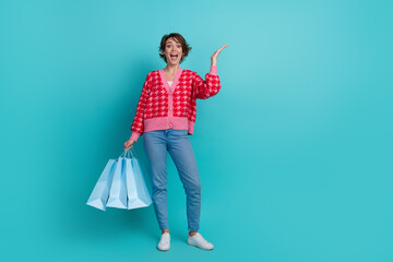 Full length photo of excited sweet lady wear red cardigan holding bargains emtpy space isolated turquoise color background