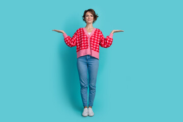 Full size photo of attractive young woman compare hold empty space dressed stylish red clothes isolated on aquamarine color background