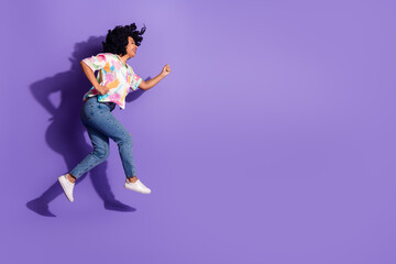 Young woman with vibrant curly hair joyfully jumps in casual fashion attire against a vibrant...
