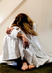 A woman in a white dress sits with her head in her arms.
