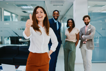 Obraz premium Happy businesswoman gesturing thumbs up with her team in modern office