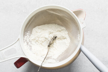 overhead view of All purpose flour in a sieve, top view of sifting baking flour into a large bowl