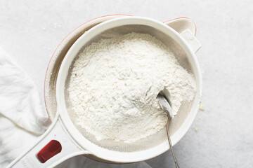 overhead view of All purpose flour in a sieve, top view of sifting baking flour into a large bowl