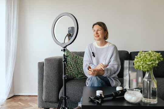 Middle-aged woman beauty blogger filming skincare product unboxing at home with ring light. User-generated content UGC for online store promotion. Vlogger live streaming. Part of a series