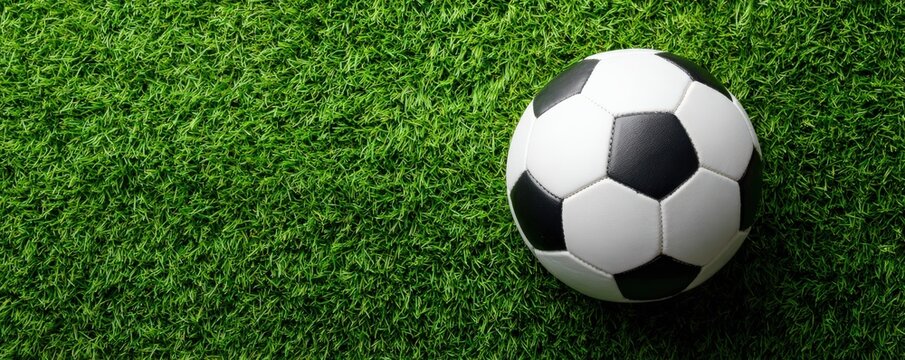 A classic black and white soccer ball rests on vibrant green artificial grass, ready for a game.