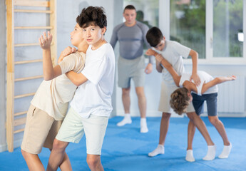 Naklejka premium Focused teen boy practicing basic protection skills with opponent in training bout during self defense course with coach in gym, trying to escape rear bear hug technique..