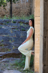 A beautiful Latin teenager with long dark hair leans her back against the stone wall of a ruined...
