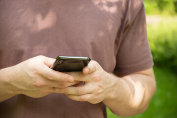 Close up of mans hands holding mobile phone in nature summer background. Check apps, focused on device, chatting, texting or browsing internet. Outdoors.