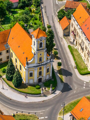 Aerial close-up of the yellow baroque-style church in Varaždin, Croatia, surrounded by curved roads and historical architecture with red roofs