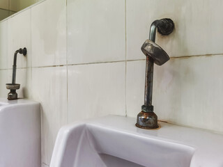 Old iron products rusted and loose from the joints attached to wall of urinal flush pipe. Old dirty...