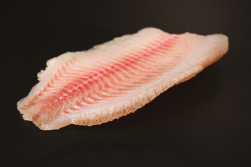 Fresh tilapia fillet on black background, top view.