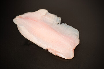 Fresh tilapia fillet on black background, top view.