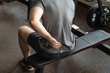 Athlete or young man sitting with pain in lower back at gym with muscle tension. Arm, inflammation...