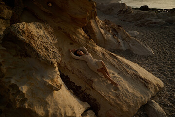 Elegant Brunette in Crochet Dress Posing by Textured Rocks at Sunset
