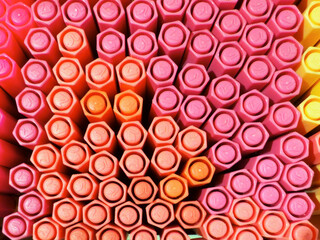 A close-up view of colorful crayons arranged in a hexagonal pattern. The crayons are primarily pink, orange, and yellow, showcasing vibrant hues and textures.