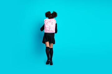 Young schoolgirl with backpack standing against a colorful turquoise backdrop, capturing the...