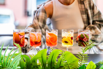 A bartender in a plaid shirt serves vibrant cocktails with fresh fruit and herb garnishes. The scene is lively, colorful, and refreshing, evoking a summer party atmosphere.